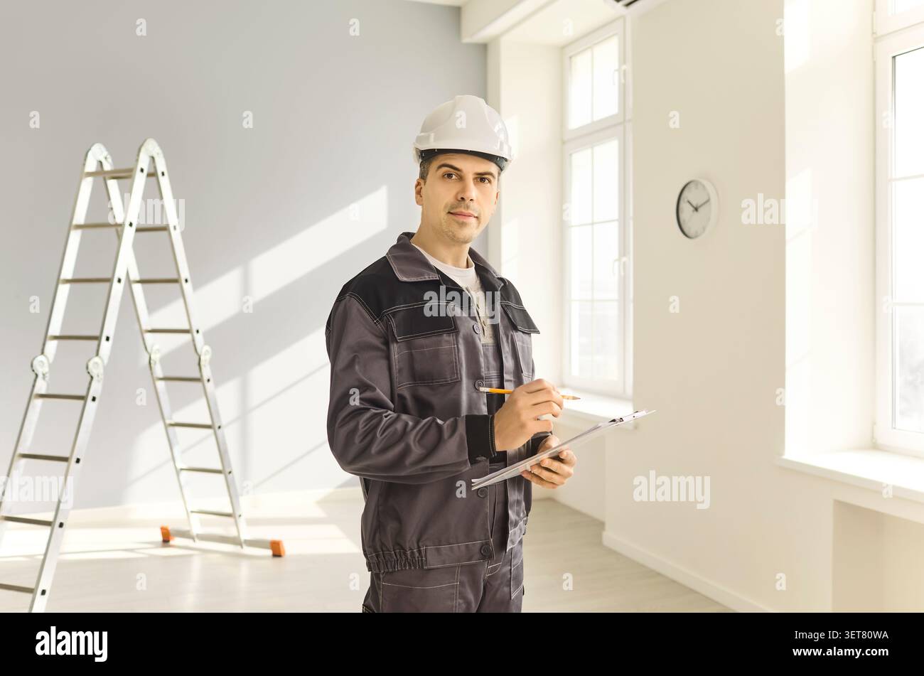 Contractor in safety helmet with clipboard assessing light modern home interior Stock Photo