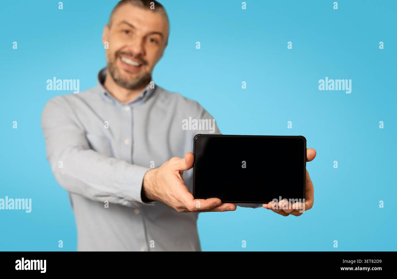 Smiling Man Holding Tablet With Blank Screen, Blue Background, Technology Concept Stock Photo