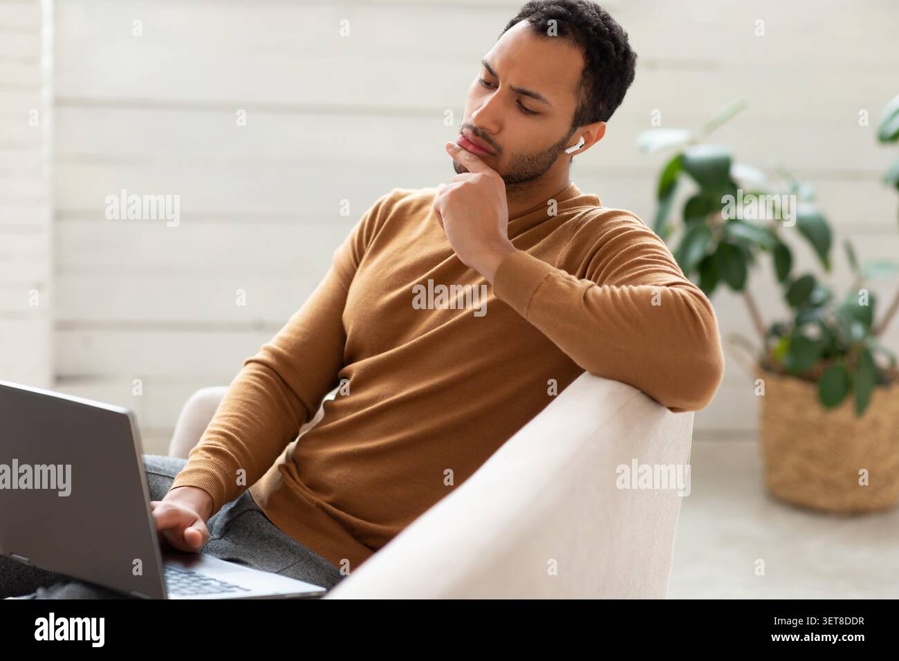 Young Man Thinking While Using Laptop In Modern Home Office, Business Concept Stock Photo