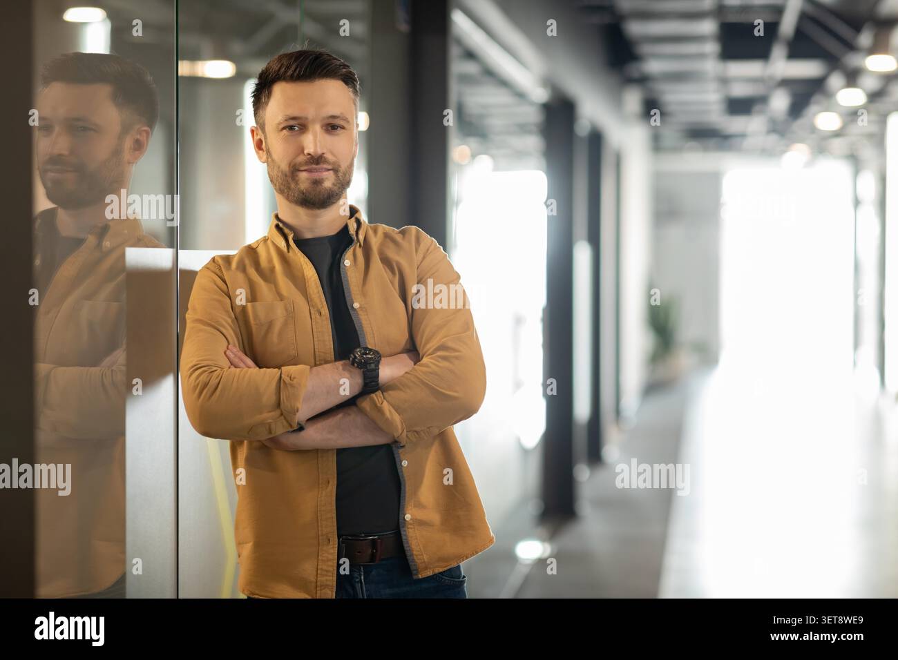 Confident Caucasian Man Standing In Modern Office, Arms Crossed, Business Concept Stock Photo