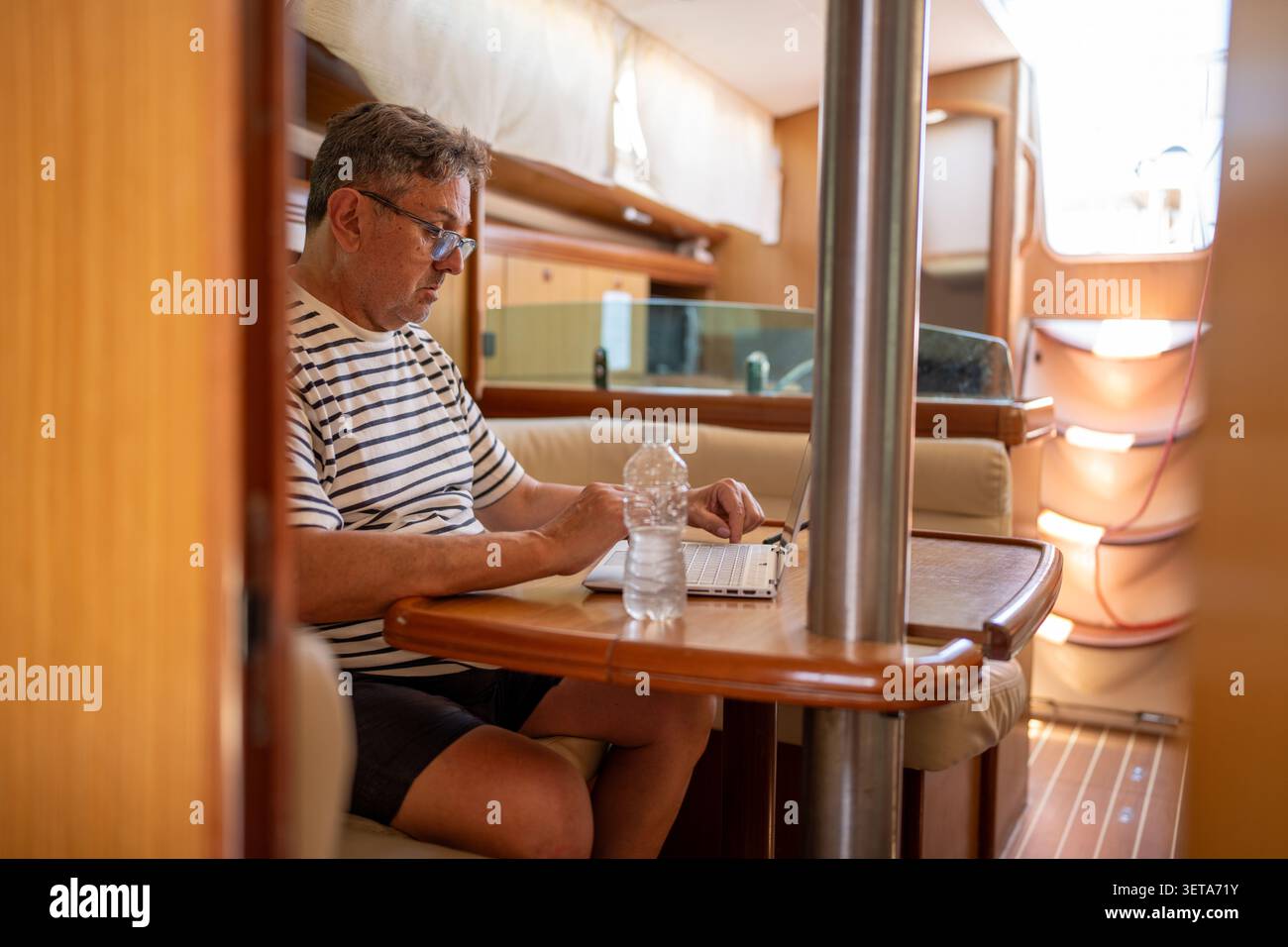 Man working remotely on laptop inside sailboat cabin Stock Photo