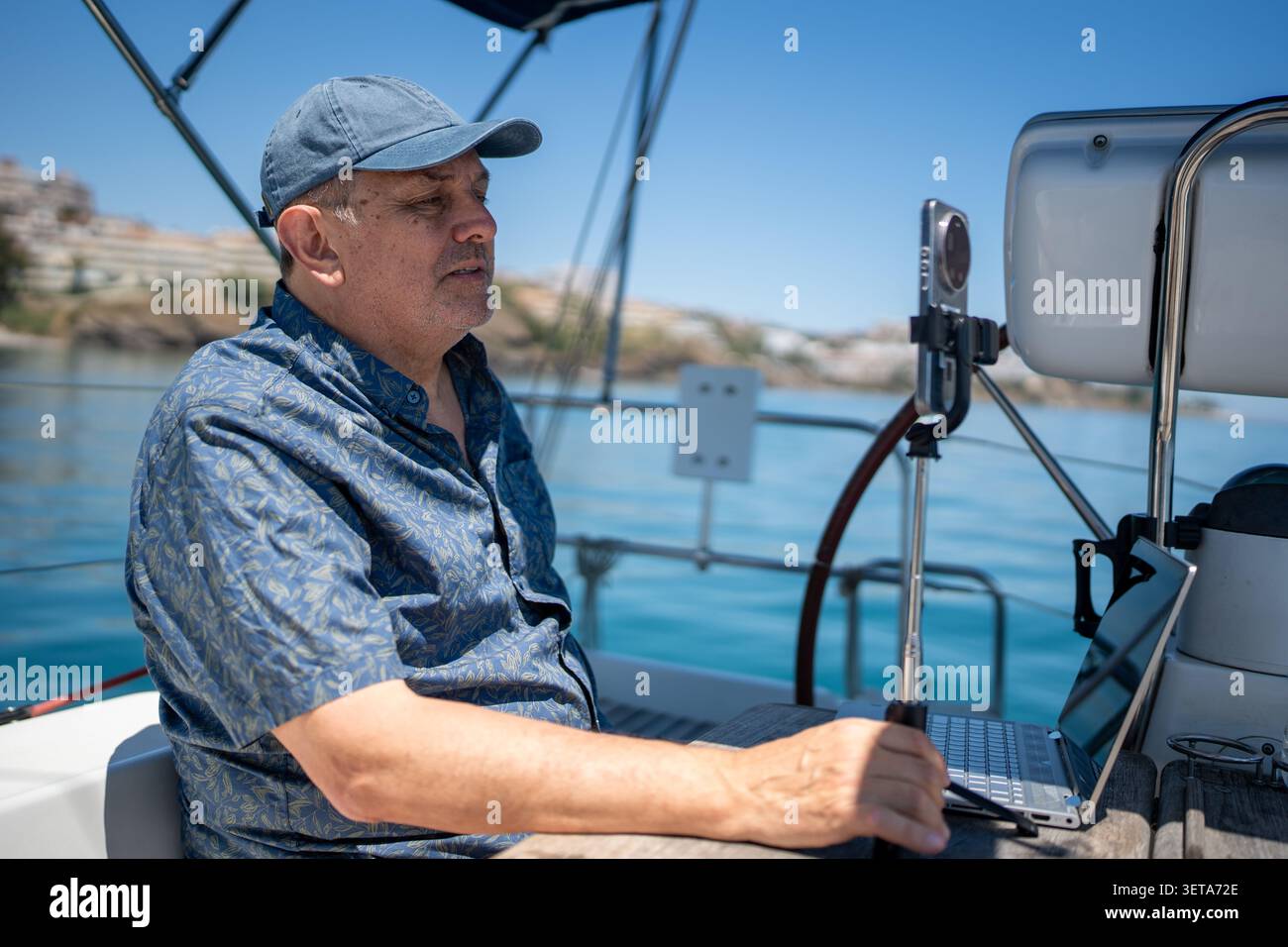 Man working remotely on sailboat using laptop smartphone Stock Photo