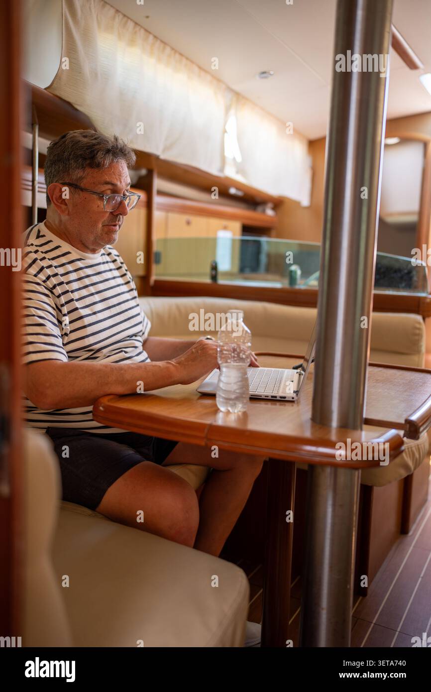 Man working remotely on laptop inside sailboat cabin Stock Photo