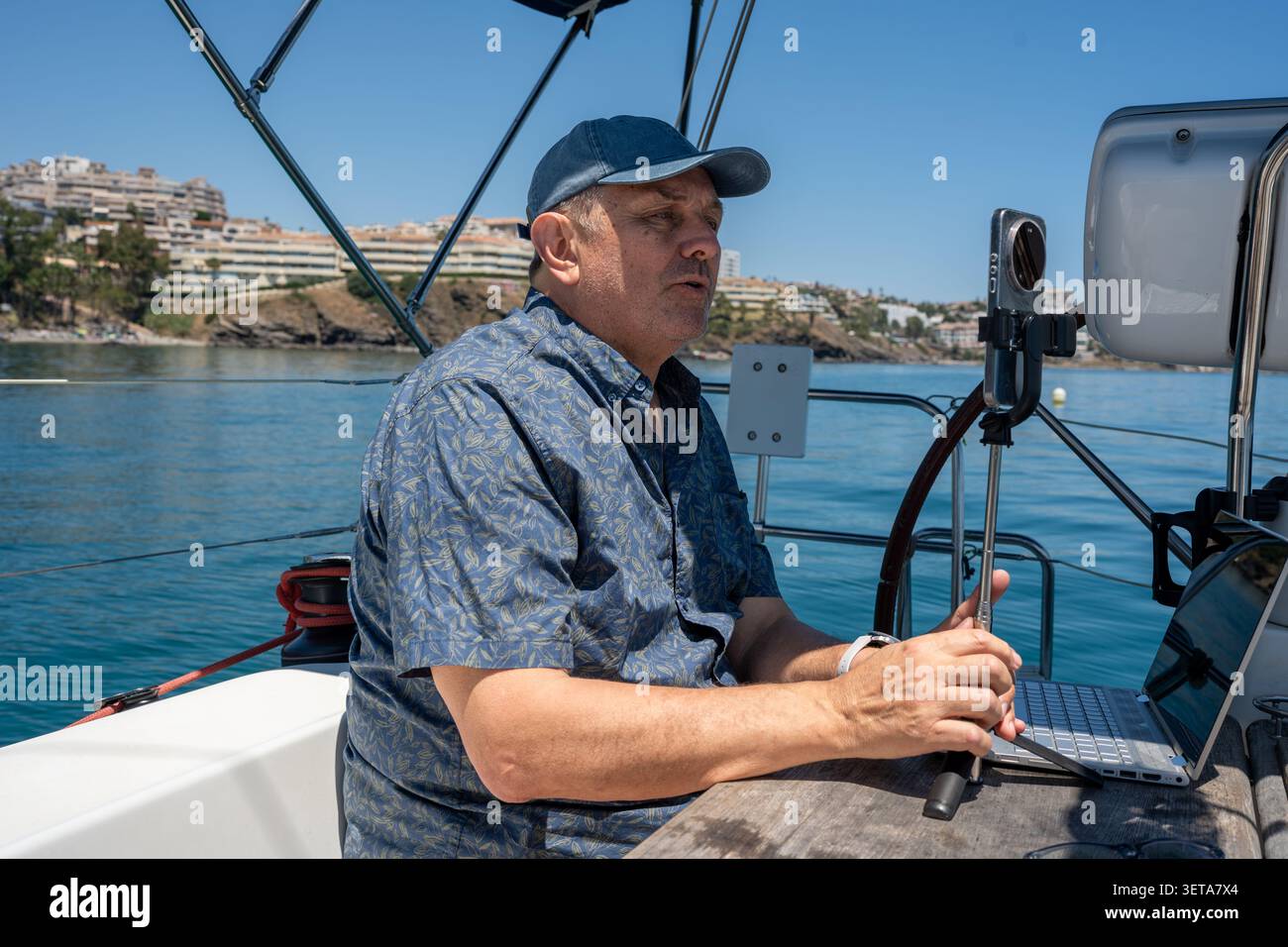 Man vlogging on sailboat while working remotely on laptop Stock Photo