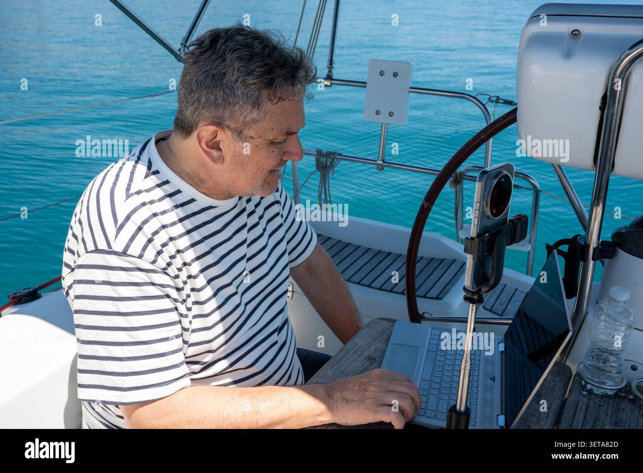 Man working remotely on sailboat while cruising ocean Stock Photo