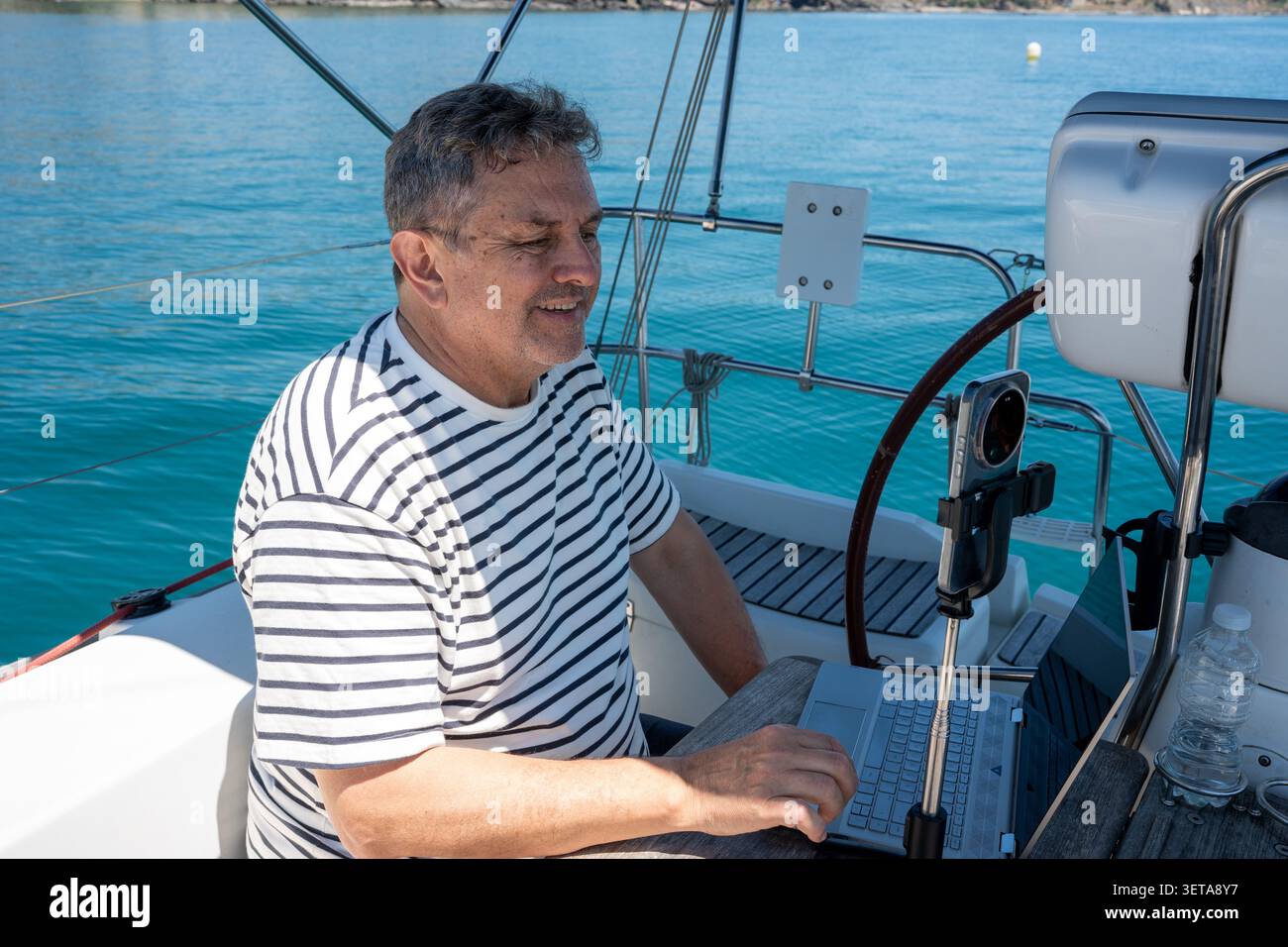 Man working remotely on sailboat by open ocean Stock Photo