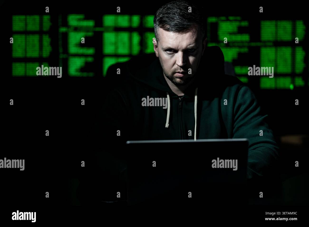 Hacker uses laptop for hacking activity. Hacker analyzes encryption and firewall system. Hacker monitors digital data flow. Hacker attempts identity Stock Photo