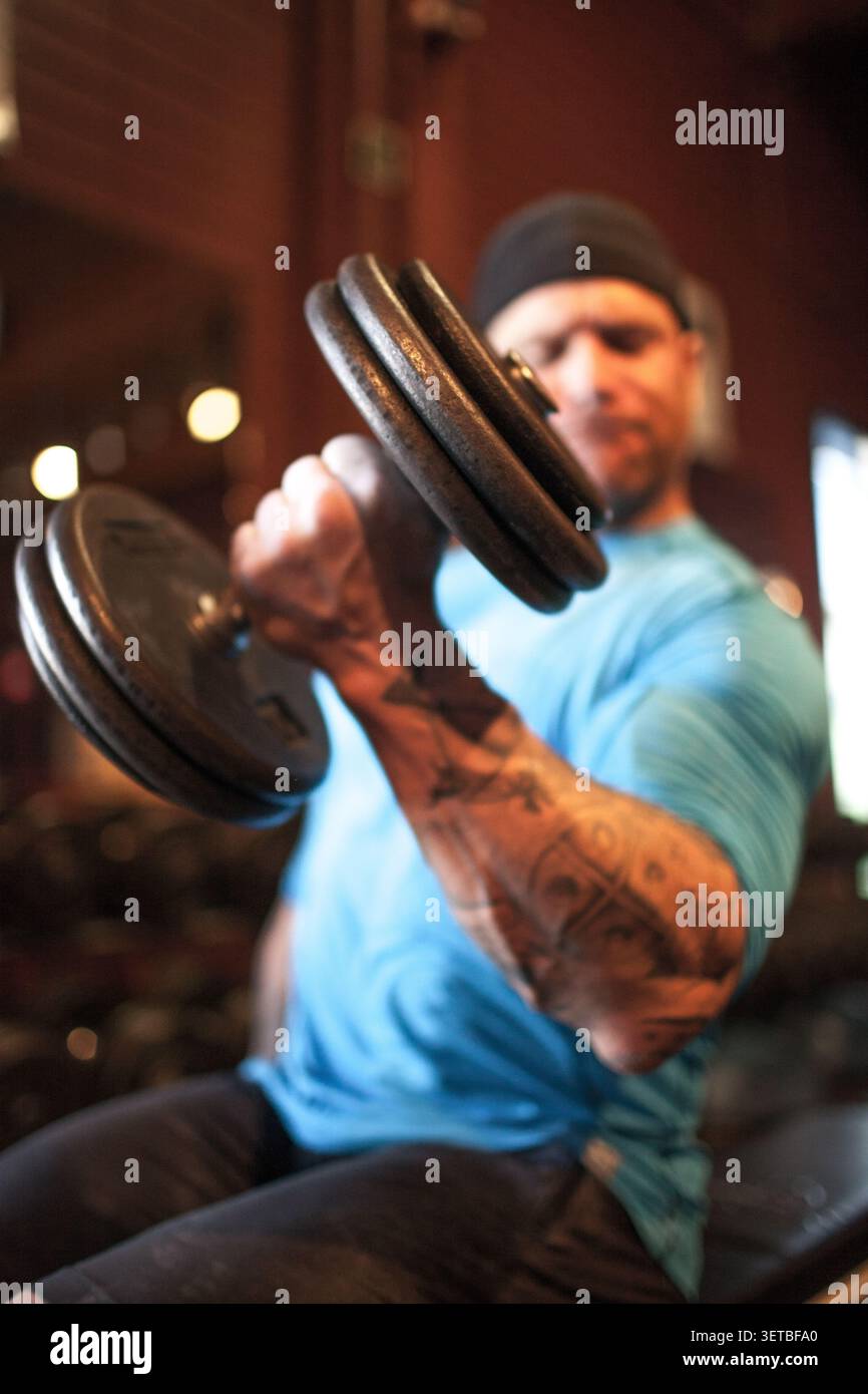 Muscular man with tattoos doing bicep curls Stock Photo
