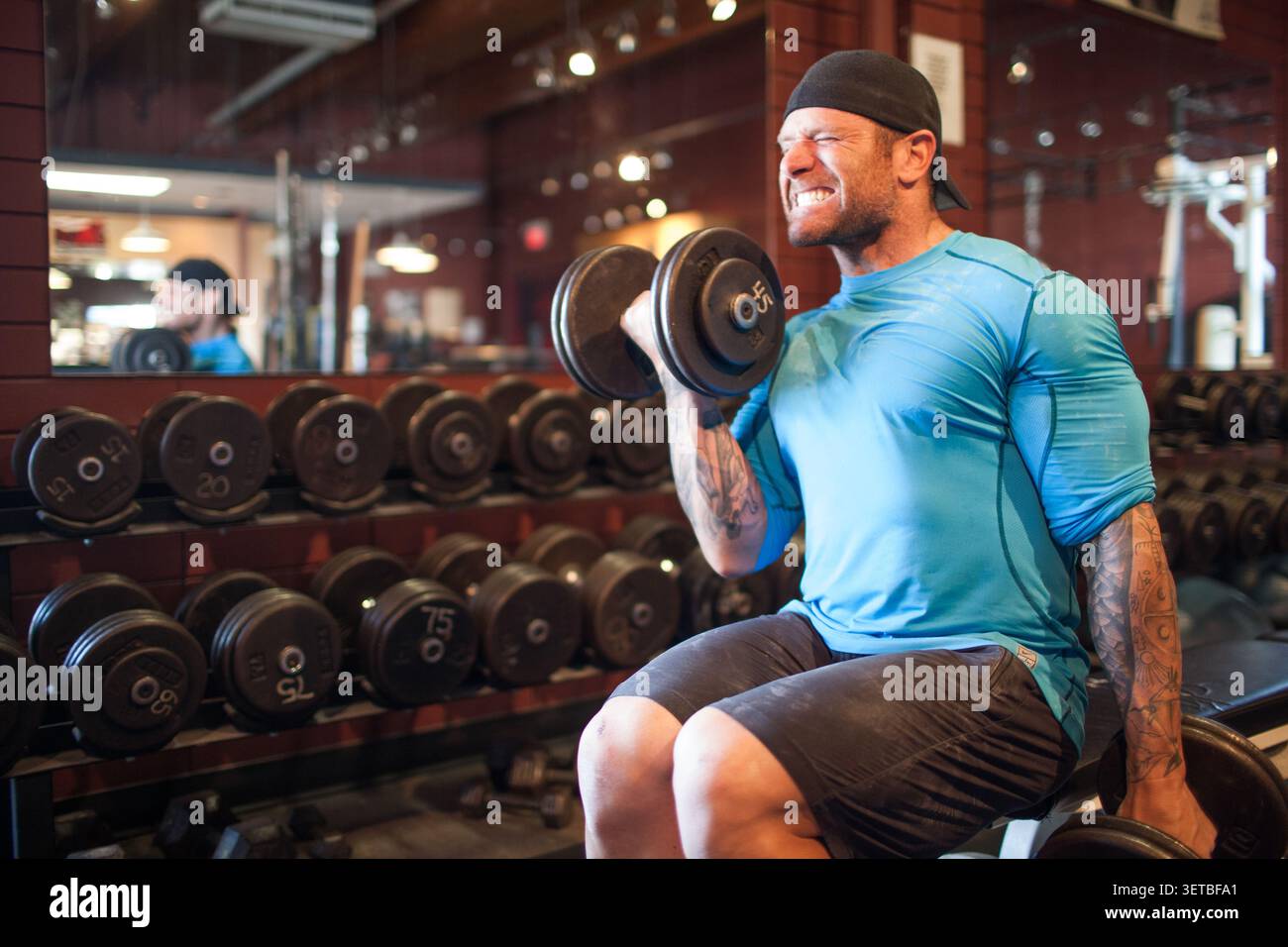 Muscular man with tattoos doing bicep curls Stock Photo