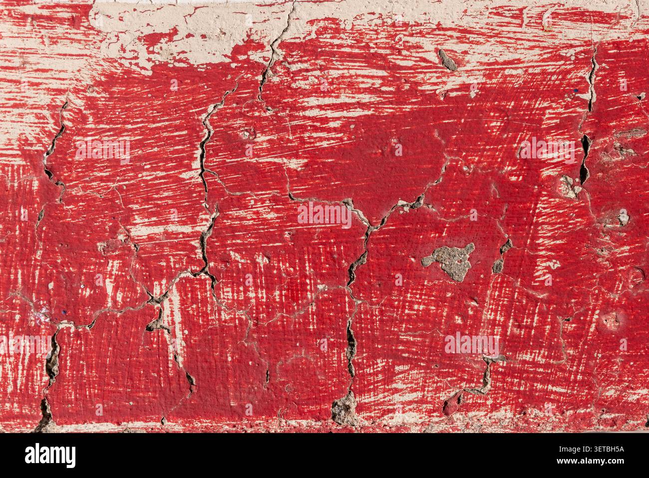 Distressed red paint cracking on an old concrete surface Stock Photo