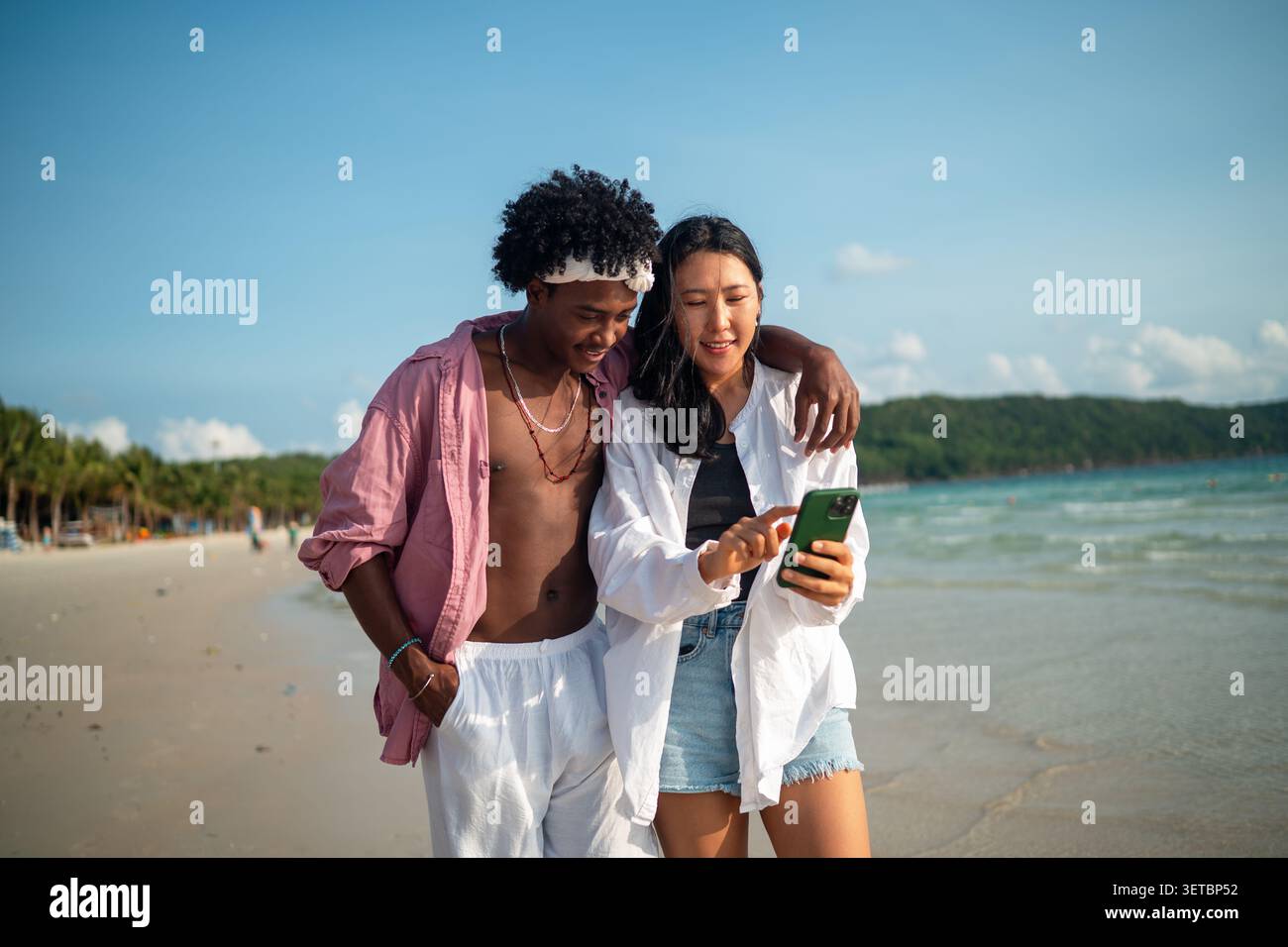 Trendy digital creator couple taking selfie by the beach, sharing travel content for social media Stock Photo
