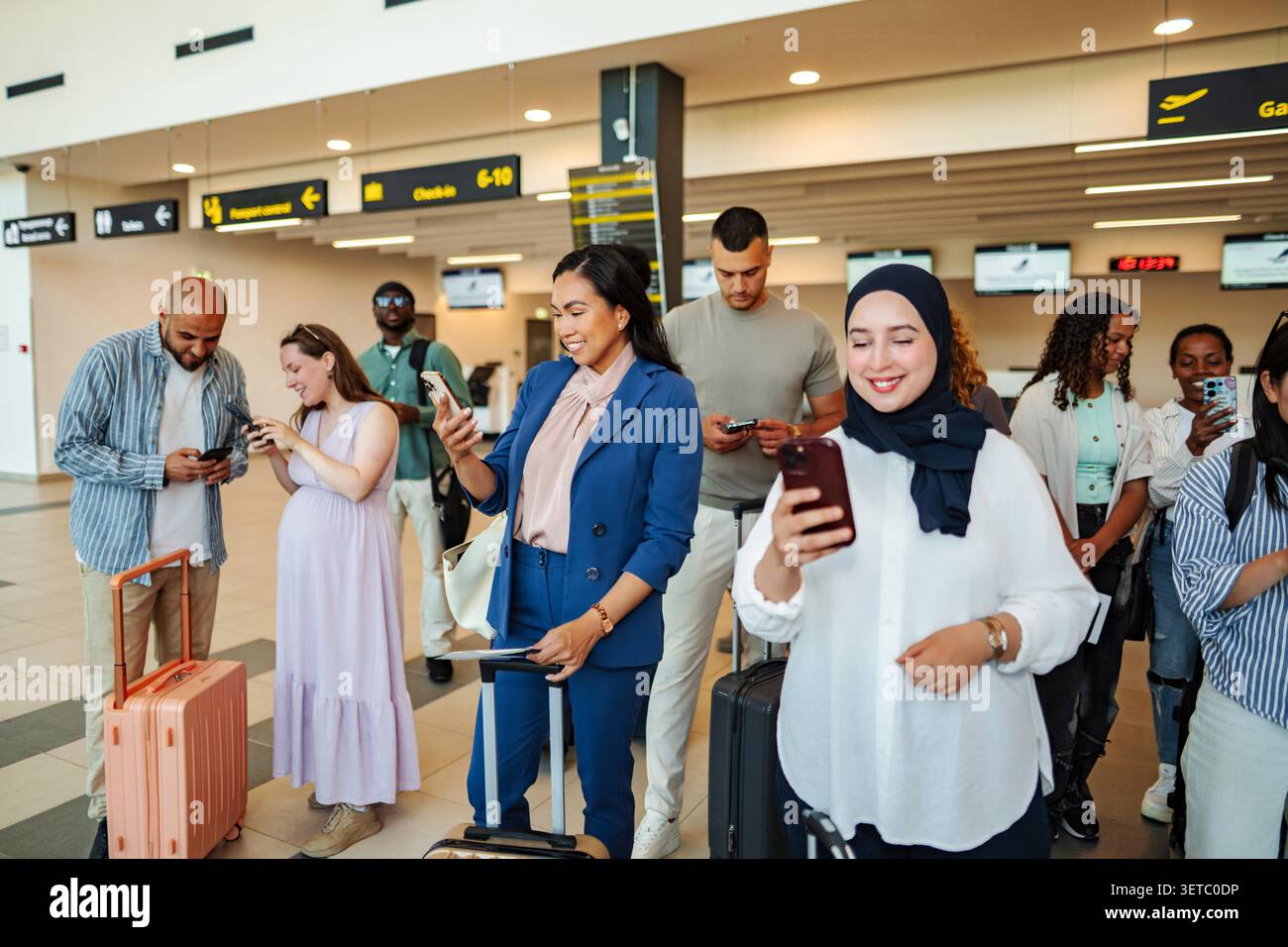 Diverse adults using mobile devices while waiting in a busy airport terminal Stock Photo