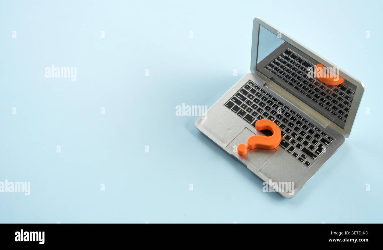 Miniature laptop computer with orange question mark on grey background Stock Photo