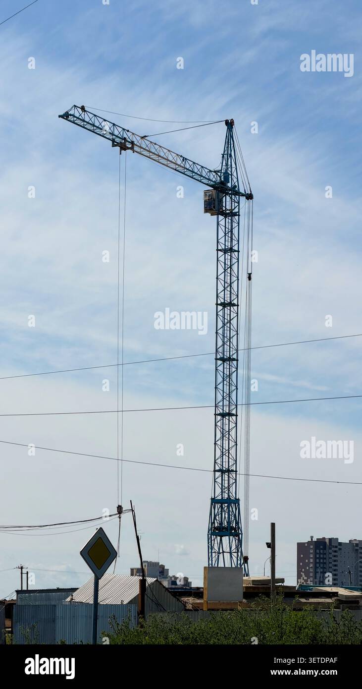 A tall blue tower crane standing against a blue sky with wispy clouds above a construction site. - Smartphone Captured Stock Image