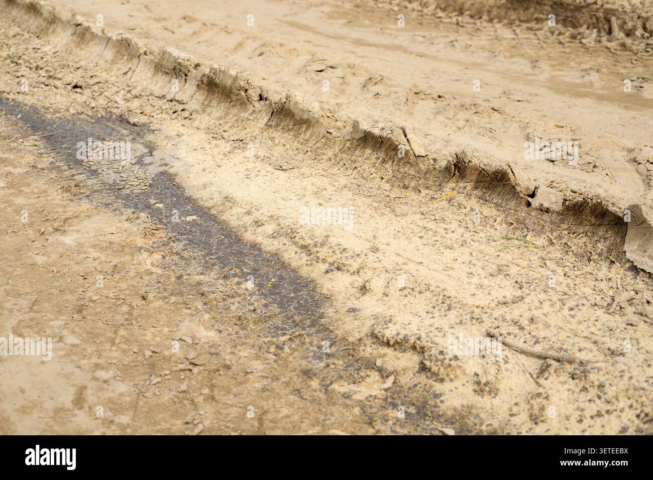 Deep tire tracks are imprinted on a dry mud road surface. Textured car wheel tread marks cover the bumpy clay and sandy ground path of a rural country Stock Photo