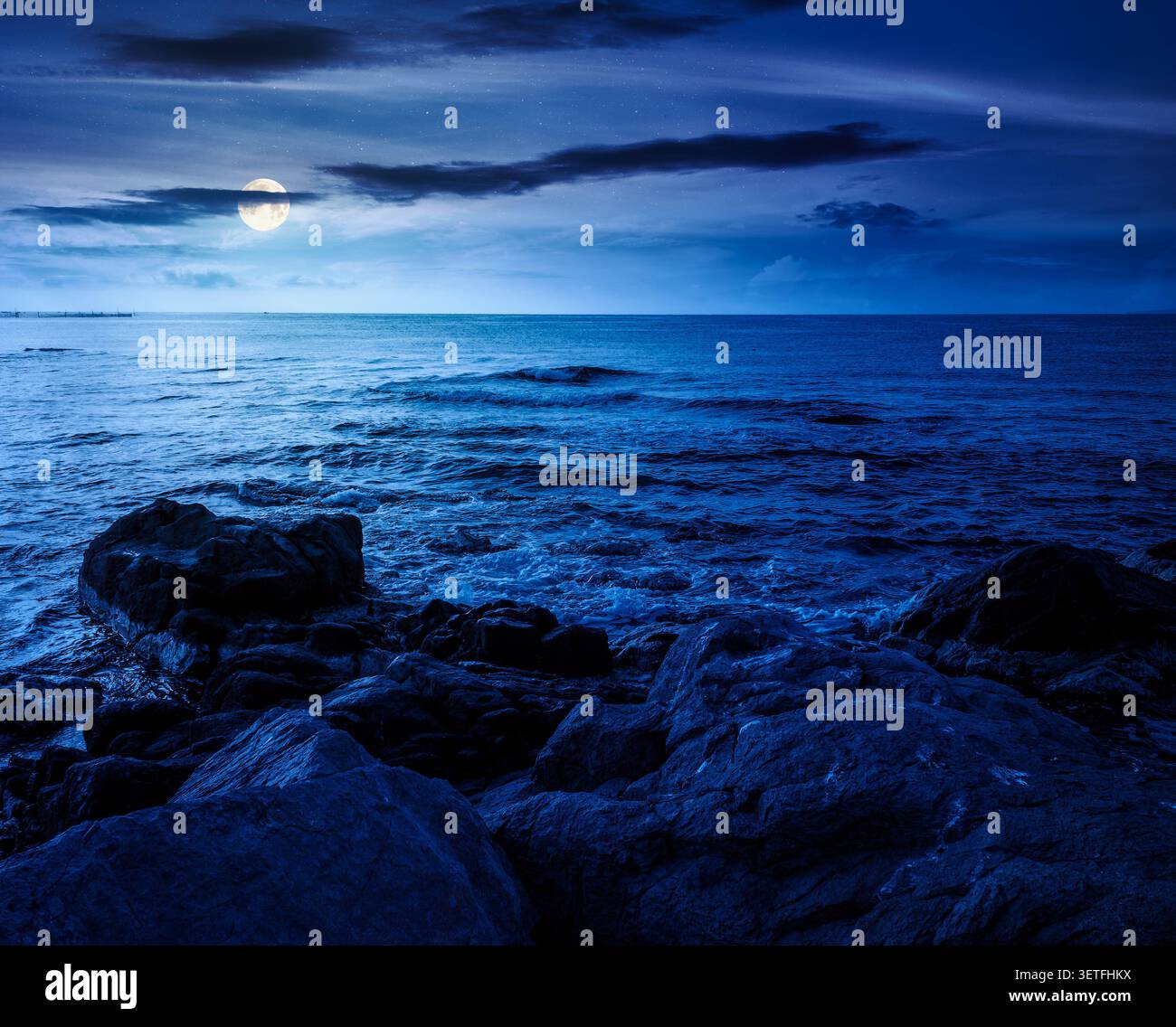sea coast with stones and rocks at night. summer vacation background. full moon over seascape with rough terrain. fantasy relaxing at the sea. mysteri Stock Photo