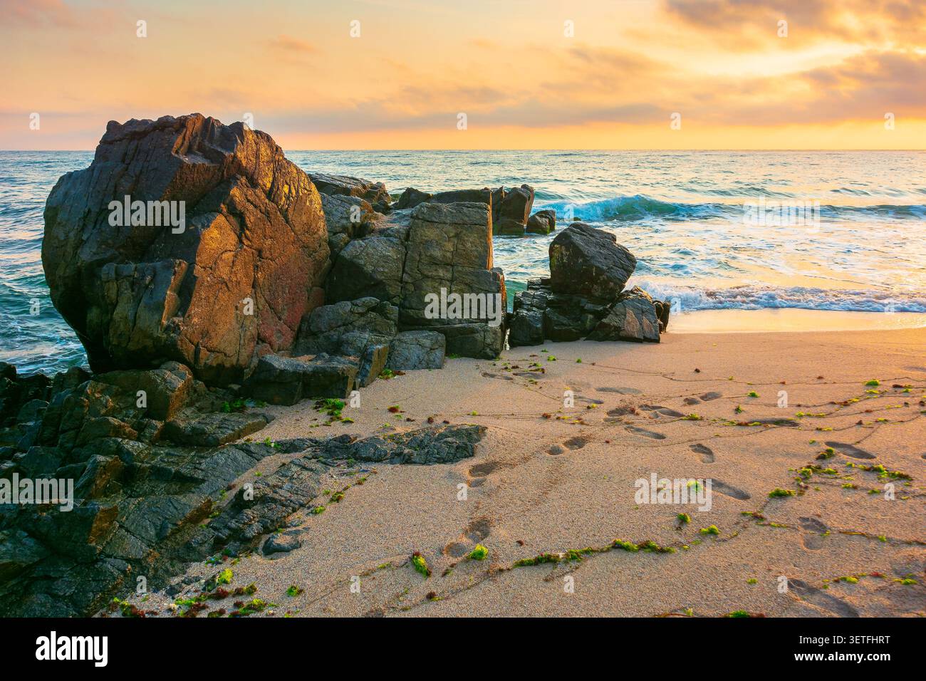 huge stones on the sandy beach at sunrise. wonderful holiday season background at the sea. clouds on the blue sky above horizon. view of waves washing Stock Photo