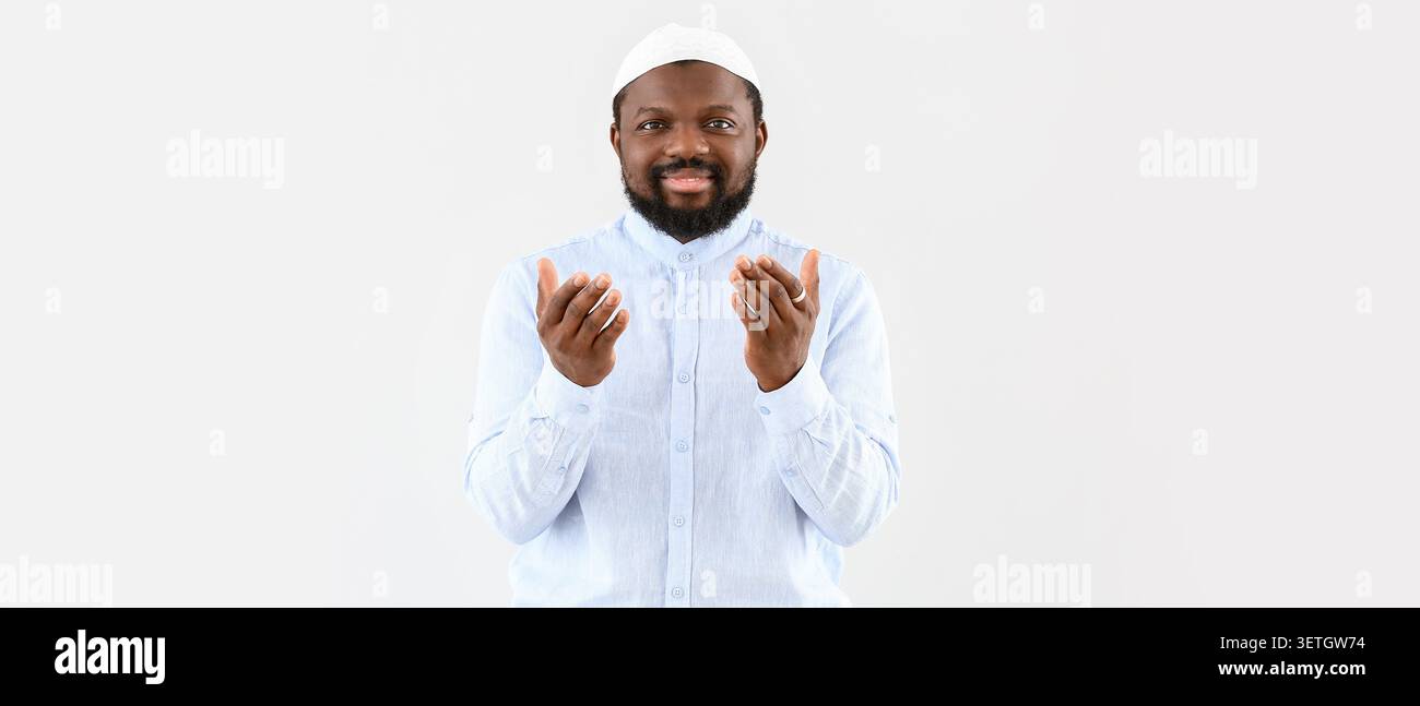 Smiling man in white shirt and cap praying with hands raised Stock Photo