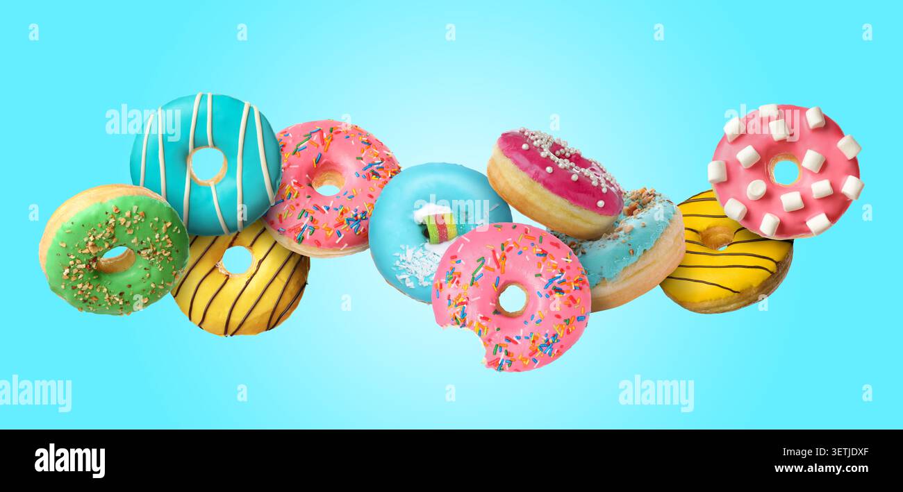 Yummy donuts covered with icing falling on light blue background Stock Photo