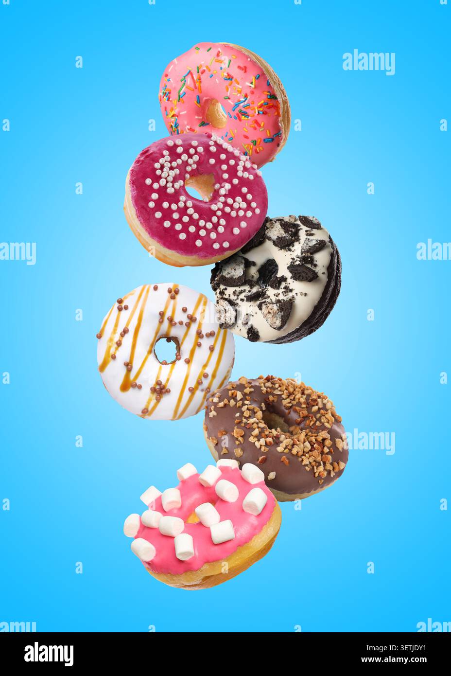 Sweet donuts covered with icing falling on blue background Stock Photo