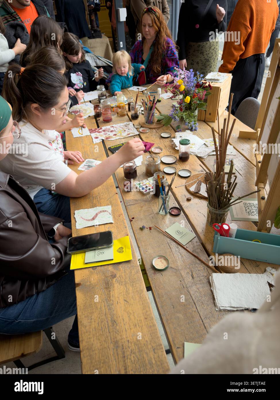 People sitting at a wooden table participating in an art & crafts workshop with natural paints & handmade paper - Smartphone Captured Stock Image
