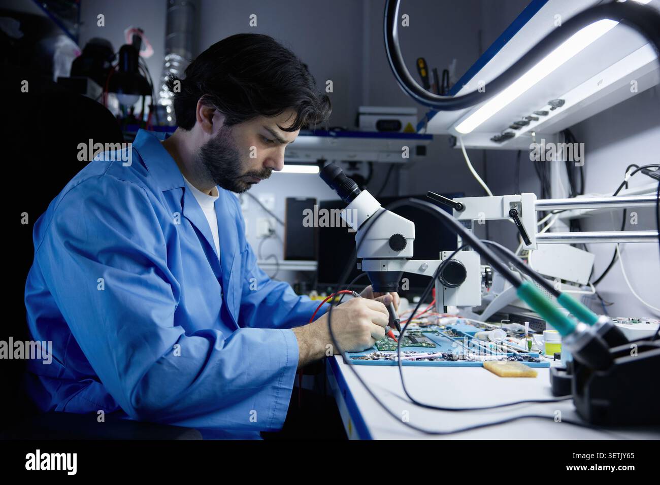 A technician working on circuit board under microscope in lab Stock Photo
