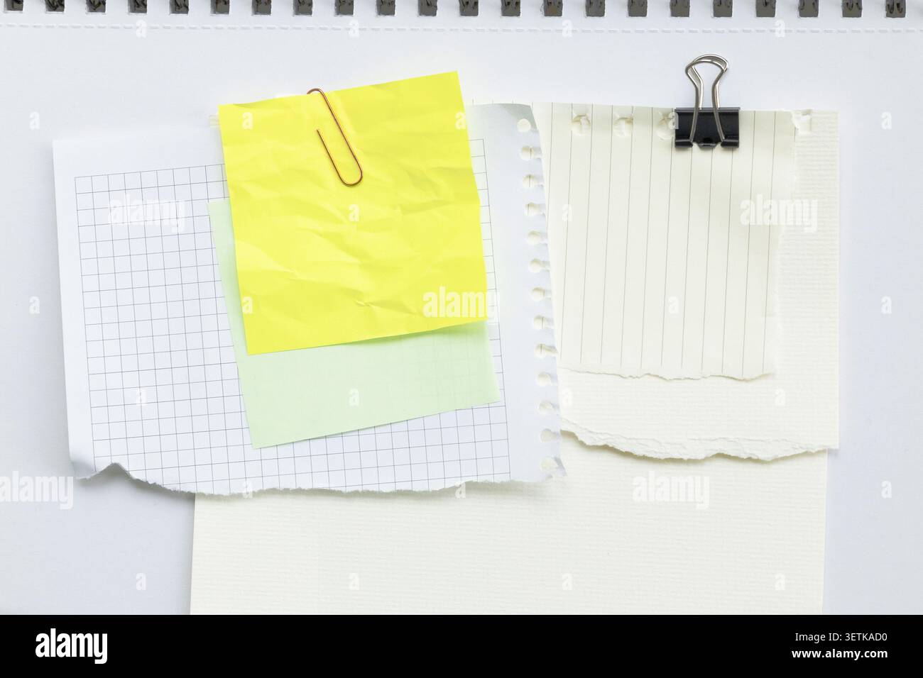 Scattered torn paper sheets collage on notebook background with clips and sticky notes. Stock Photo