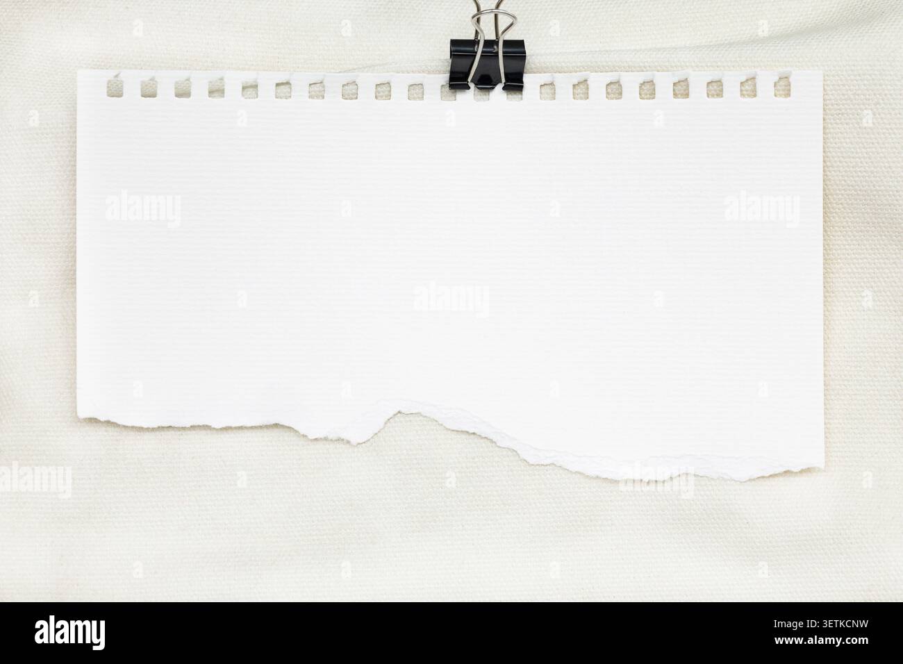 Blank torn notebook paper sheet with binder clip on canvas background. Stock Photo