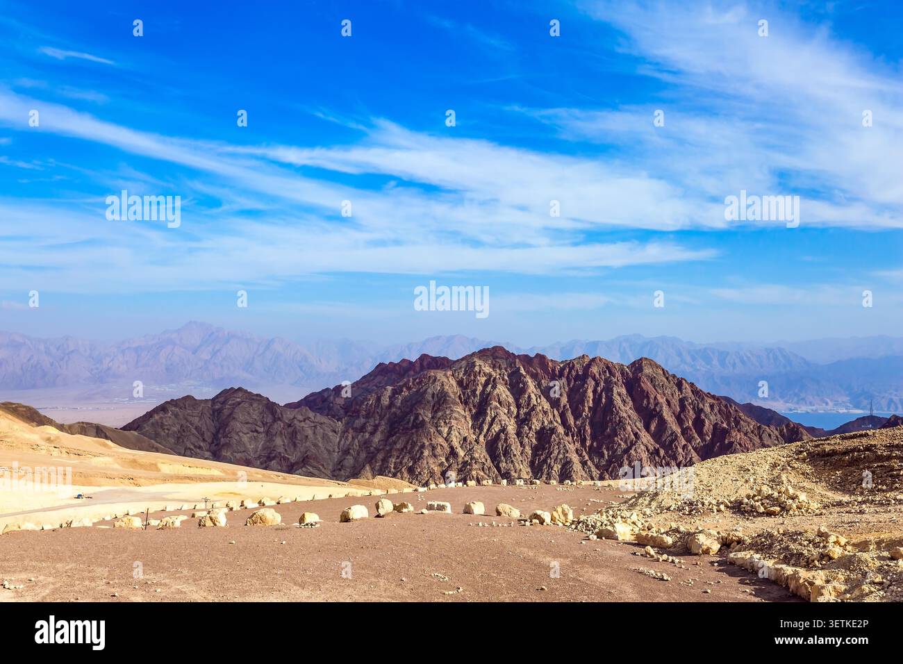 The dirt road is marked with stones. The Eilat Mountains, Israel. The iron in the rocks gives the mountains black-purple and red colors. Stock Photo