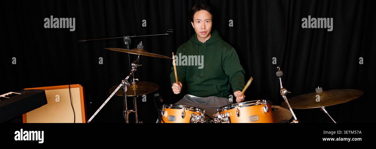 Talented young Asian man plays drums with passion in a vibrant recording studio environment. Stock Photo