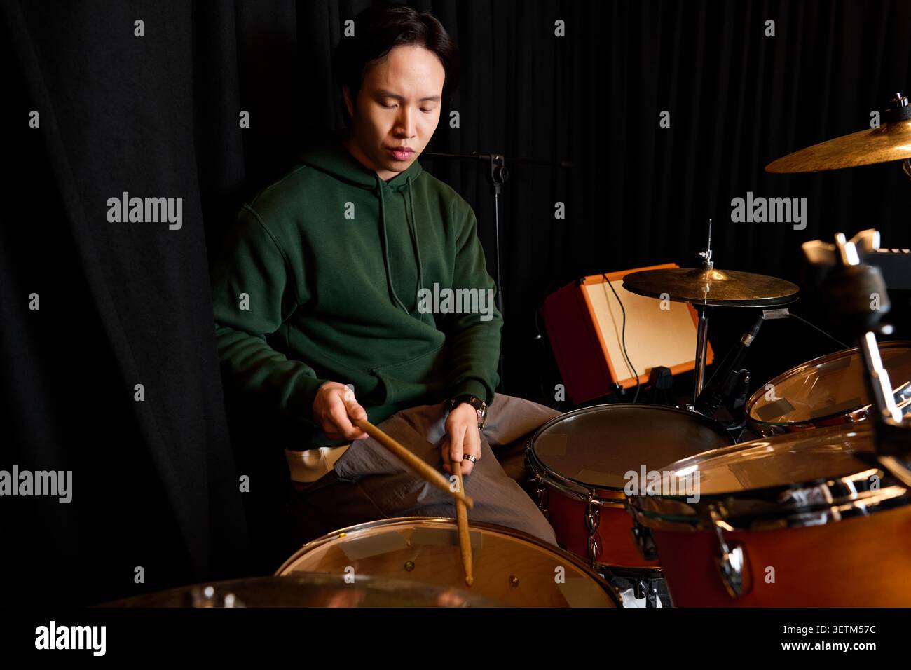 Focused young man plays the drums, creating rhythmic magic in a lively studio atmosphere. Stock Photo