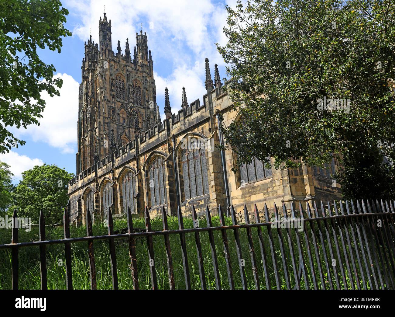The ornate medieval tower and south side of St Giles Parish Church rise above the leafy churchyard in central Wrexham / Wrecsam city centre Stock Photo