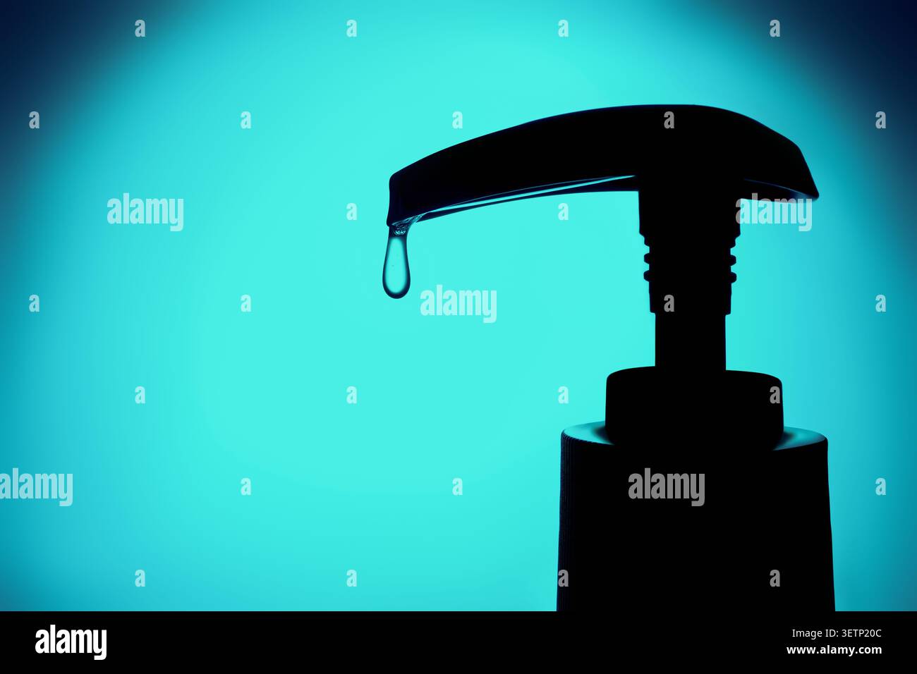 Soap dispenser head in silhouette dispensing single drop of liquid on turquoise background Stock Photo