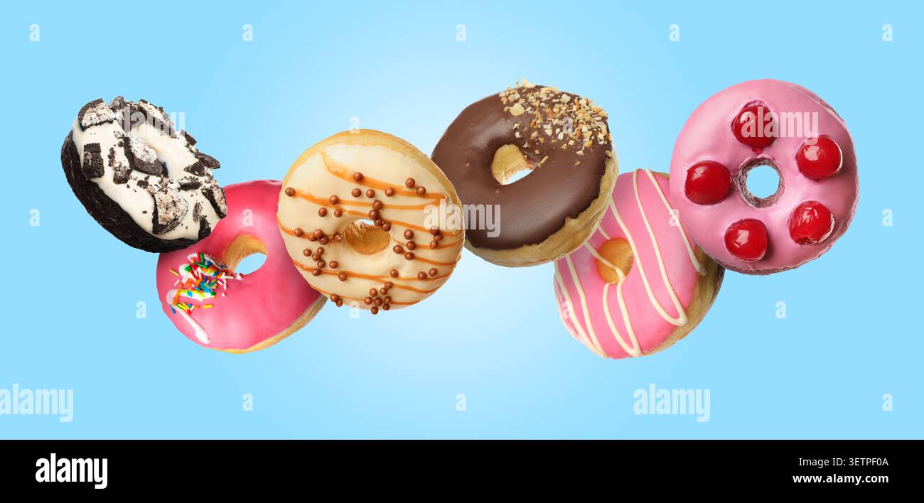 Yummy donuts covered with icing falling on light blue background Stock Photo