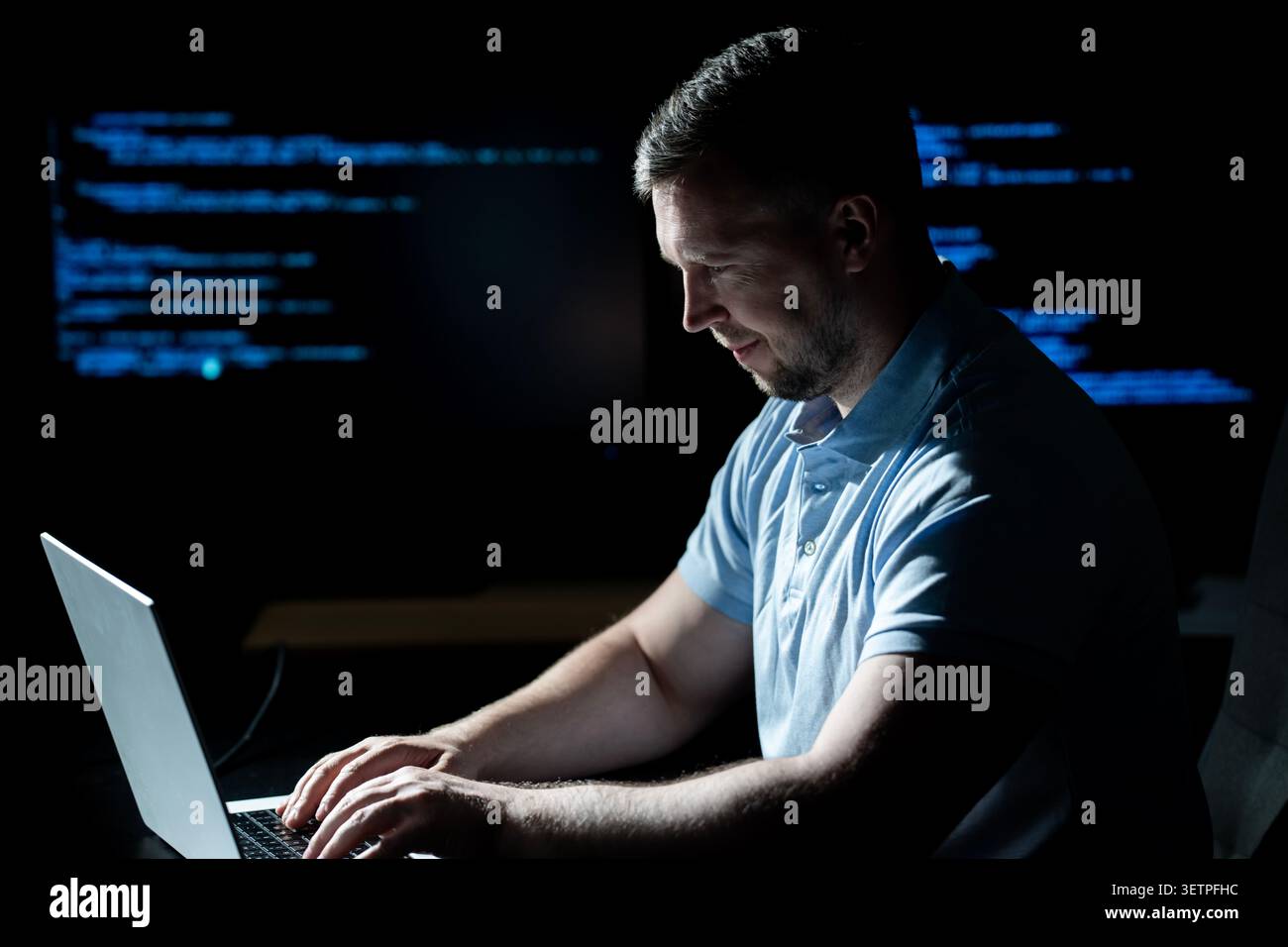 Hacker operates laptop in dark office. Hacker analyzes code screen carefully. Hacker monitors system logs for access. Hacker executes cyber attack on Stock Photo