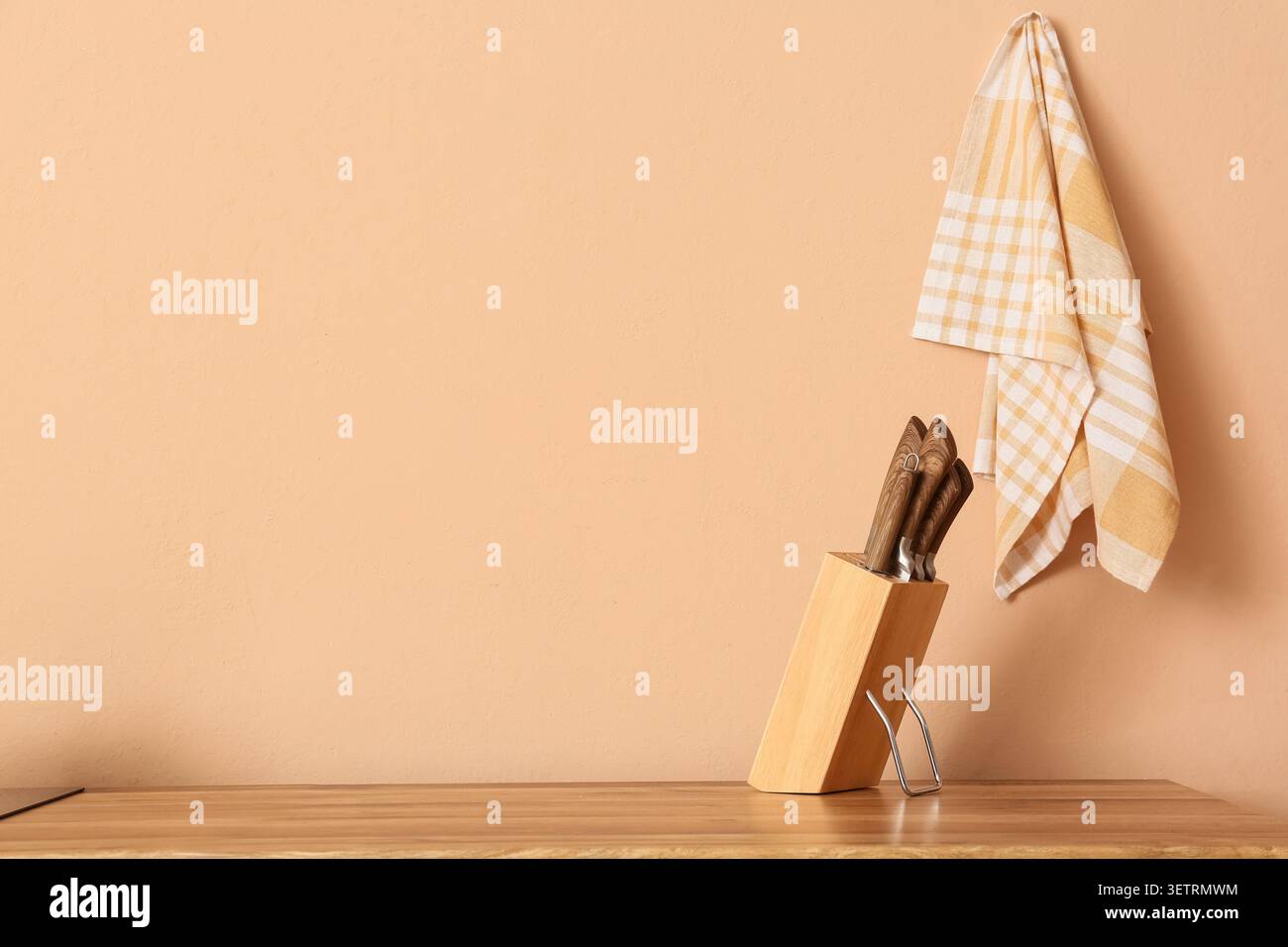 Wooden knife block with knives and hanging kitchen towel on beige wall Stock Photo