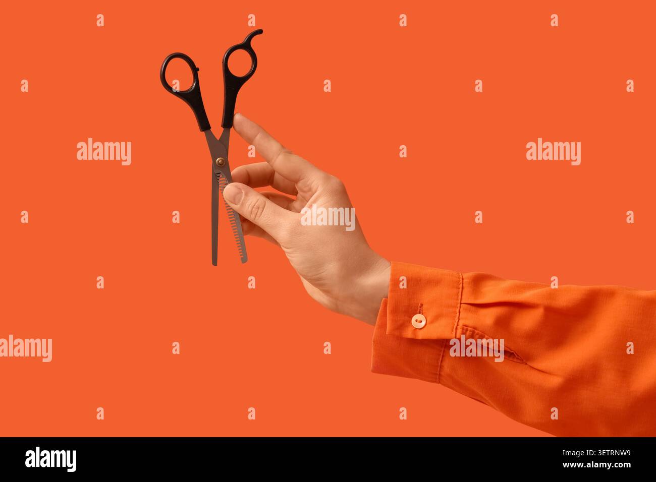 Hand holding thinning scissors on orange background Stock Photo