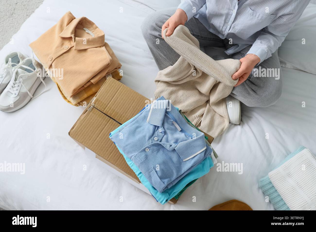 Person folding clothes on bed with cardboard box Stock Photo