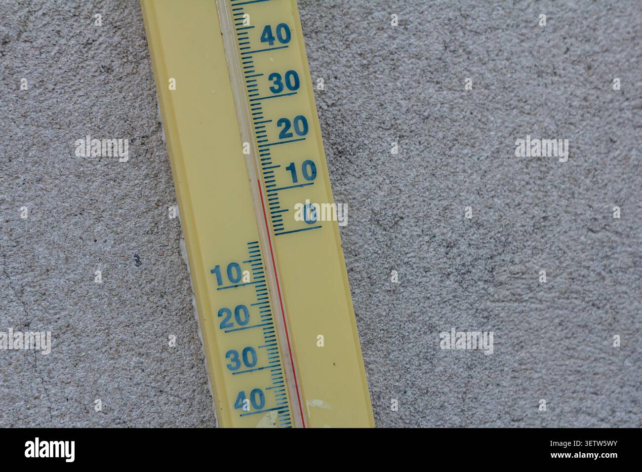 A bright yellow thermometer displays temperature readings on a gray textured surface indicating warm weather conditions in an outdoor setting on a sun Stock Photo