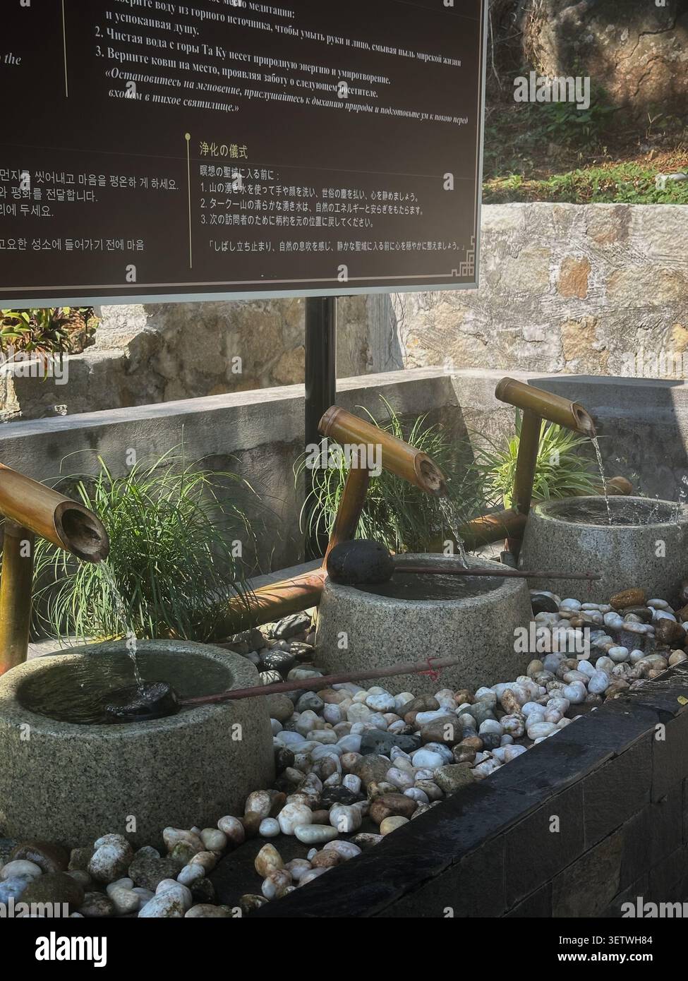 Traditional bamboo water fountain with stone basins for ritual purification. A serene asian temple fountain featuring bamboo pipes flowing into stone Stock Photo