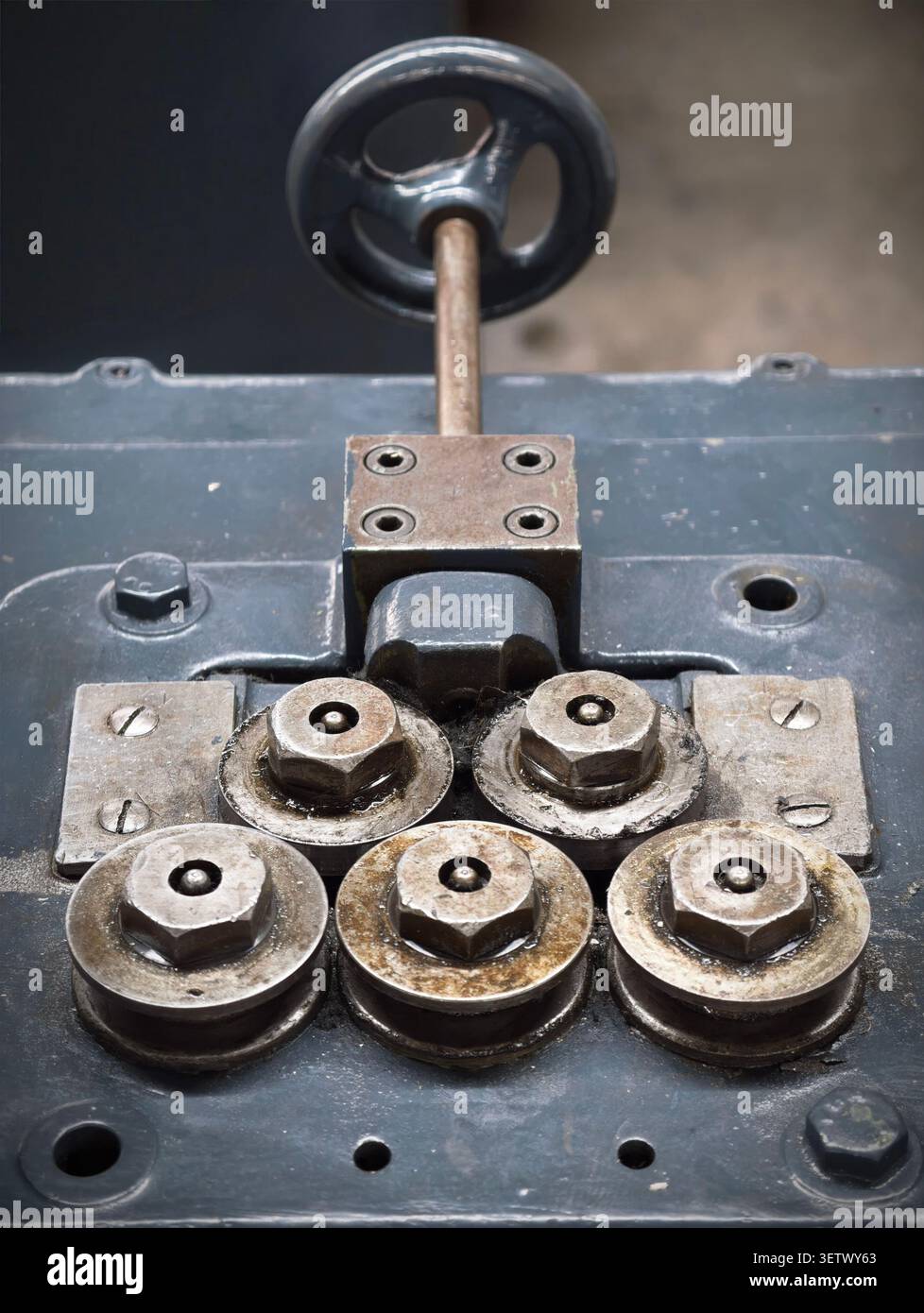 Worn industrial roller assembly with multiple metal rollers, hex nuts, washers, and mounting plates fixed to painted machinery base, showing grease, r Stock Photo