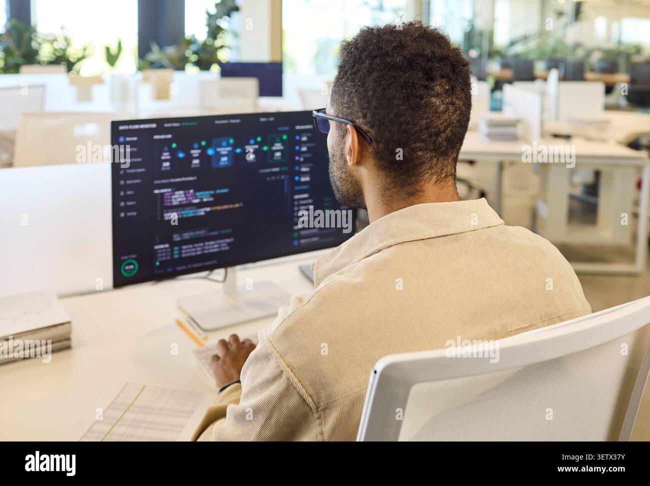 Male programmer coding at desktop computer in bright modern office workspace Stock Photo