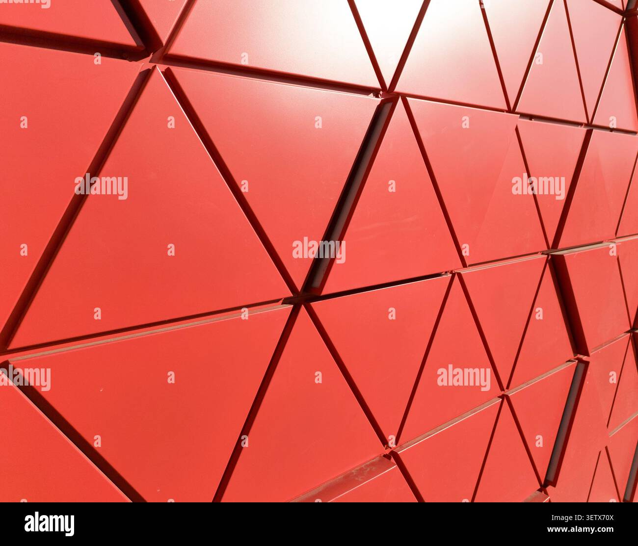 Red geometric facade with triangular panels forming dynamic architectural pattern. Surface structure creates depth and bold composition. Concept of mo Stock Photo