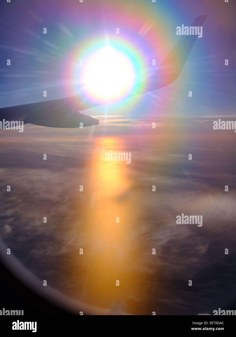 A view from plane window of a dramatic Sun set over Sweden during the midnight sun over the wing of the plane flaring rainbow colours into the camera Stock Photo