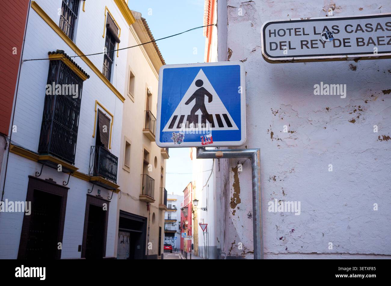 A pedestrian crossing sign blue with a person walking across a zebra crossing in Seville Spain between a narrow street. Stock Photo