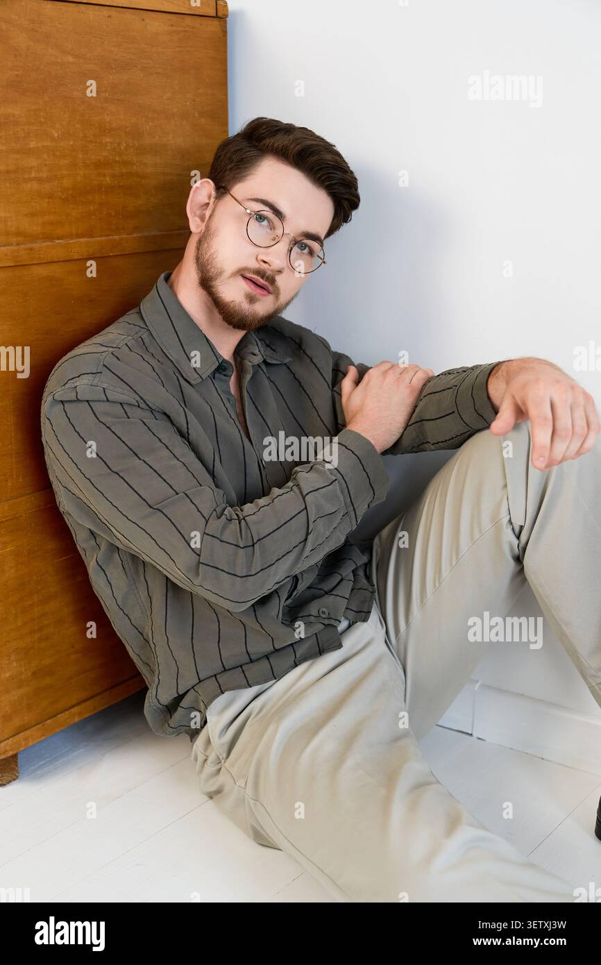 Charming young man with beard poses thoughtfully in a studio with wooden backdrop Stock Photo