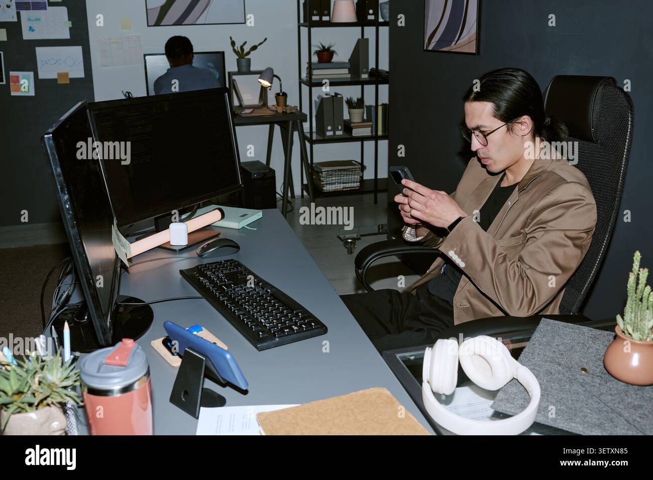 Asian Man Checking Smartphone during Late Night Office Work Stock Photo