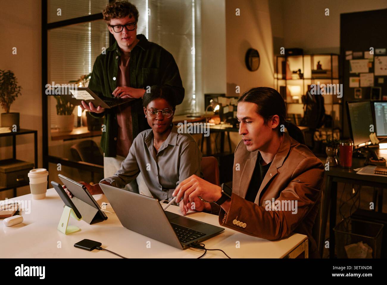 Diverse Coworkers Reviewing Laptop Data during Evening Office Meeting Stock Photo