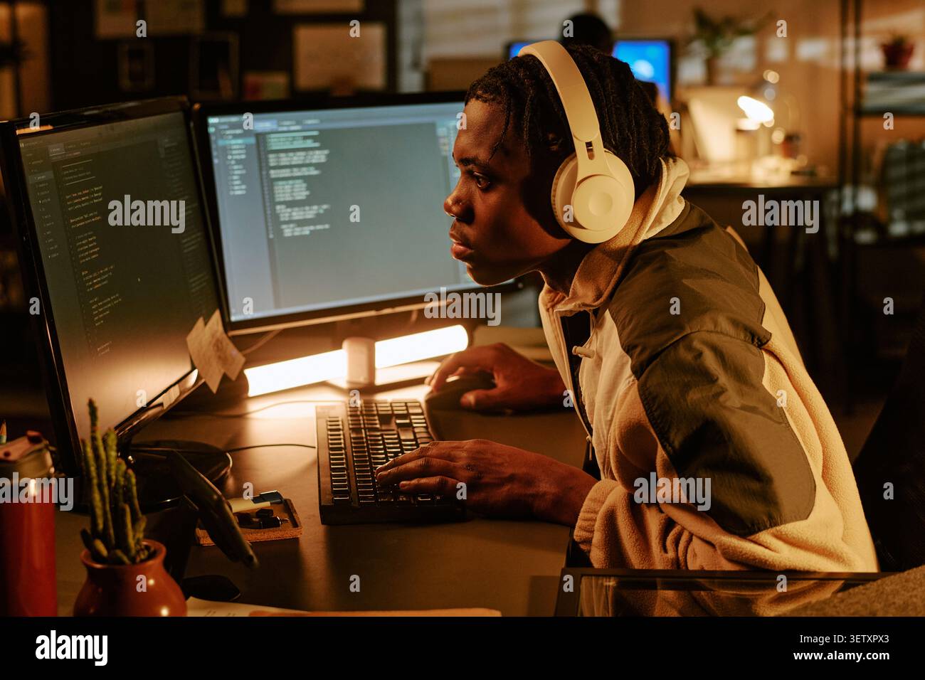 Black Man Coding at Dual Monitors in Office at Night Stock Photo