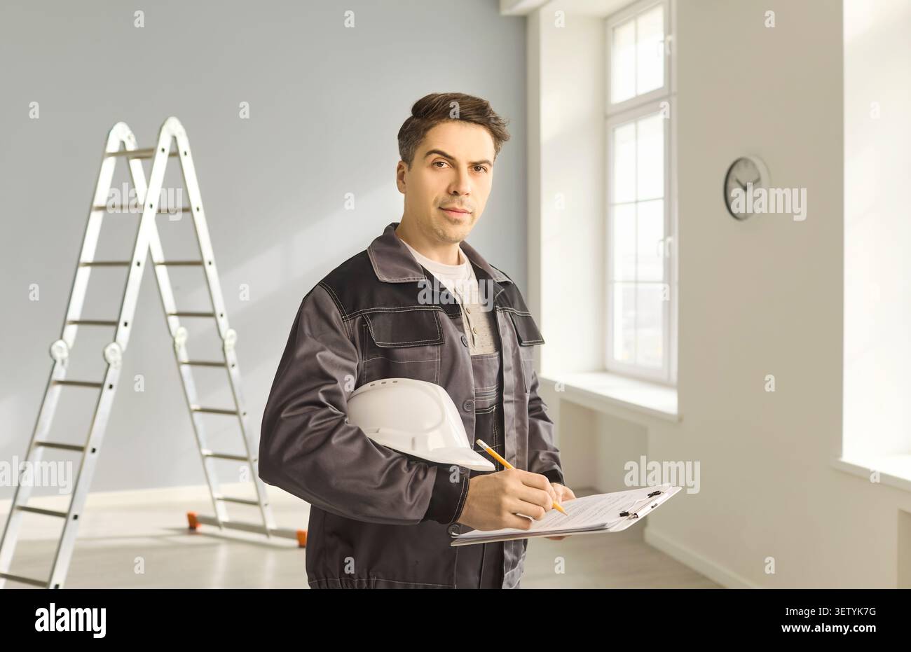 Builder inspector with clipboard and helmet making notes during room renovation Stock Photo